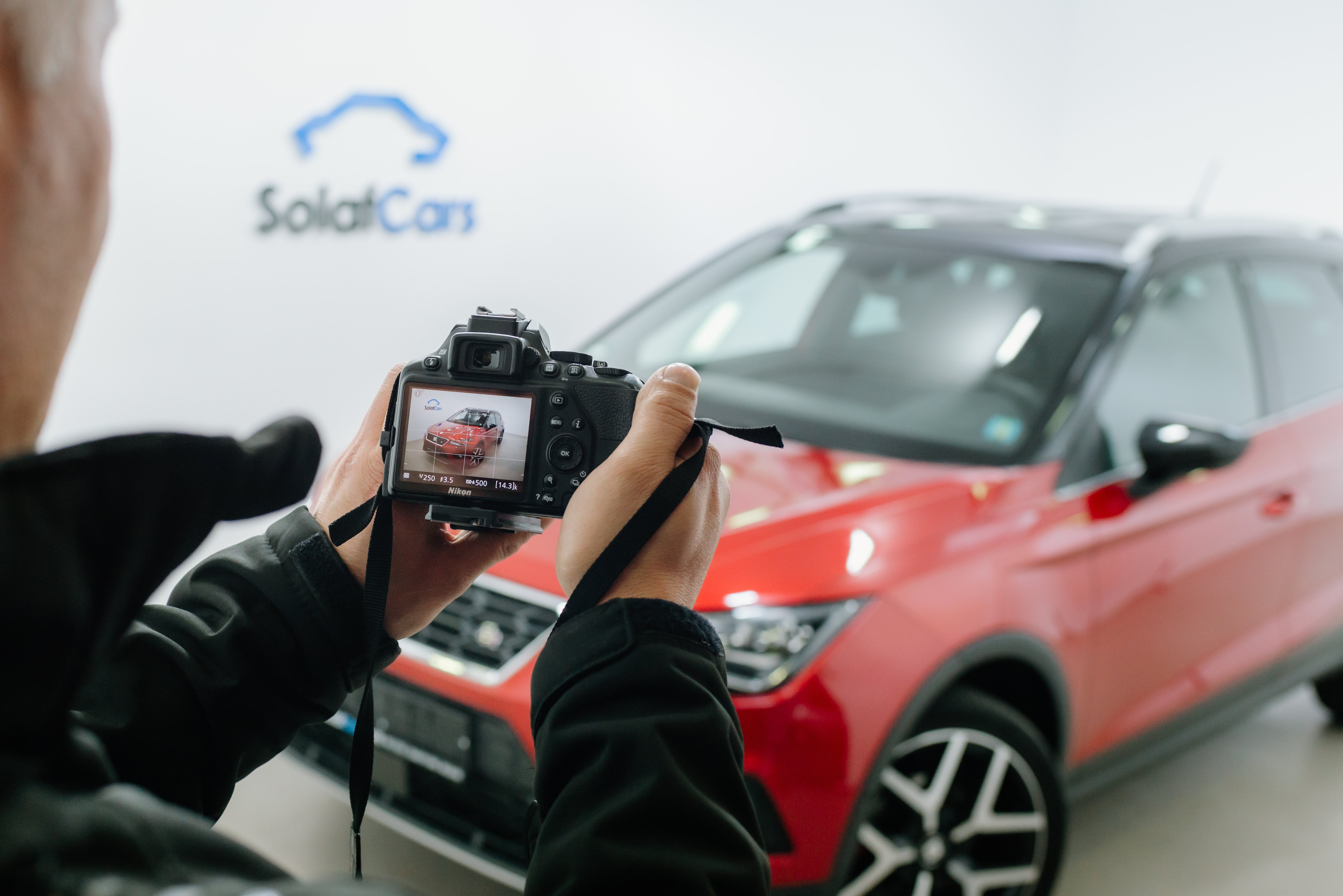Gros plan d'un homme prenant une photo sur un appareil photo reflex numérique d'une voiture rouge dans un studio photo